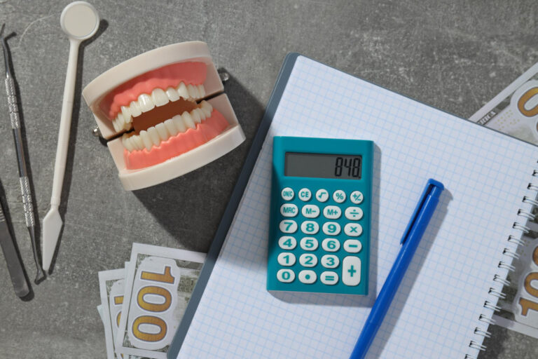 A dental model, calculator, and dental tools placed on a notebook with graph paper and $100 bills, symbolizing dental cost planning and budgeting for dental procedures.